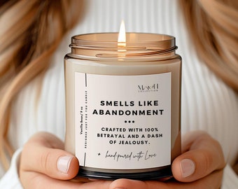 May include: A brown glass candle with a white label that reads "Smells Like Abandonment... Crafted with 100% Betrayal and a dash of Jealousy. Hand-poured with Love."