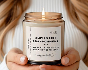 May include: A brown glass candle with a white label that reads "Smells Like Abandonment... Made with 100% Regret and a Hint of Freedom. + hand-poured with Love"