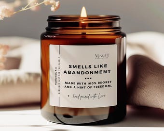 May include: A brown glass candle jar with a white label that reads "HAVIN COLLECTION SMELLS LIKE ABANDONMENT ... MADE WITH 100% REGRET AND A HINT OF FREEDOM. + hand-poured with Love DESIGNED JUST FOR YOU CANDLE Vanilla Bean/ 9 oz"