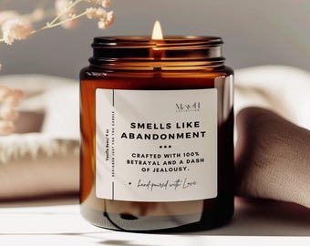 May include: A brown glass candle jar with a white label that reads "Smells Like Abandonment... Crafted with 100% Betrayal and a dash of Jealousy. + hand-poured with Love"