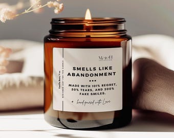 May include: A brown glass candle jar with a white label that reads "Smells Like Abandonment... Made with 101% Regret, 50% Tears, and 200% Fake Smiles. + hand-poured with Love"