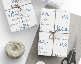 May include: Three white gift boxes with blue and gold text. The text on the boxes reads "Making Life More Fun Since 1985" and "Oliver".