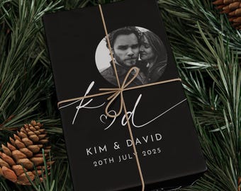 Puede incluir: Caja de regalo negra con un círculo blanco que contiene una foto en blanco y negro de una pareja. La caja está atada con cuerda y tiene el texto "K&D" en blanco cursivo con un símbolo de corazón. Debajo de la foto, el texto "KIM & DAVID 20TH JULY 2025" está impreso en blanco.