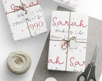 May include: White gift wrap with a red and gold star pattern. The text "Sarah Making Life More Fun Since 1990" is printed on the wrap.