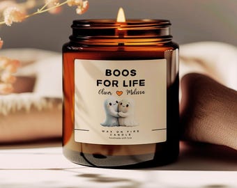 May include: A lit candle in a brown glass jar with a label that reads "Boos For Life" with two cartoon ghosts. The label also includes the names "Oliver" and "Melissa" and the words "Wax on Fire Candle".
