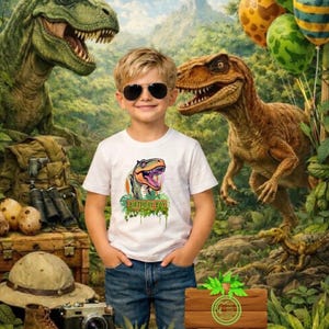 Puede incluir: Un joven con gafas de sol y una camiseta blanca con un gráfico de dinosaurio y el texto "BIRTHDAY BOY". La imagen presenta un fondo de jungla con ilustraciones de dinosaurios, globos y un letrero de madera.