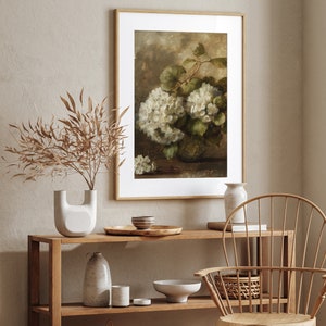 May include: A framed print of a still life painting featuring a bouquet of white hydrangeas in a vase. The painting is set against a brown background and has a vintage aesthetic.