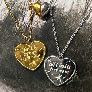 May include: Gold and silver heart-shaped necklaces with chain links. One gold pendant reads "i feel like myself right now" and the other silver pendant reads "all i feel is free now". A two-tone heart pendant is also visible.