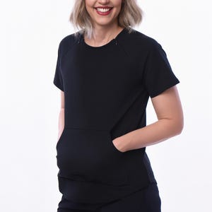 May include: Black short-sleeved top with a large front pocket and matching shorts. The top has a crew neck and raglan sleeves. The shorts have a scalloped hem. The outfit is made of a soft, solid black fabric.