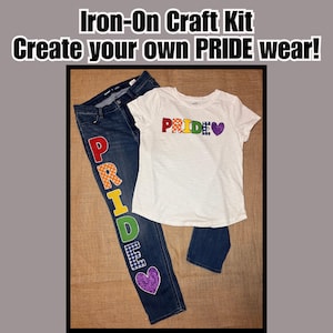 May include: An iron-on craft kit with the text "Iron-On Craft Kit Create your own PRIDE wear!" includes a white t-shirt and blue jeans. The jeans have the word "PRIDE" spelled out in colorful patches. The t-shirt also has the word "PRIDE" in colorful patches.