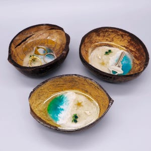 May include: Three coconut shell jewelry dishes with resin art. One dish holds gold rings. The other two feature beach scenes with blue, white, and green resin. One has a key, the other has a starfish and turtles.