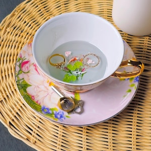 Puede incluir: Una taza de cerámica blanca con un asa negra y el texto "But First, Coffee" en negro, con una fuente de estilo manuscrito. La taza está sobre una superficie blanca.