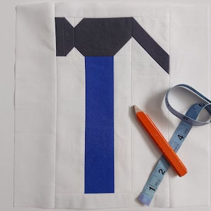 May include: A white fabric square with a blue and gray hammer design. A blue measuring tape and an orange pencil are on the fabric.