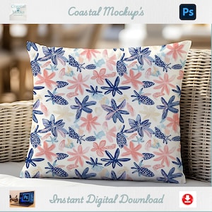 May include: A square decorative pillow with a white background and a repeating pattern of blue, pink, and light blue floral and sea-themed designs. The pillow is displayed on a wicker chair.