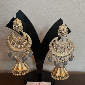 May include: A pair of gold earrings with gray beads and white pearls. The earrings have a crescent moon shape with intricate designs and a bell-shaped dangle.