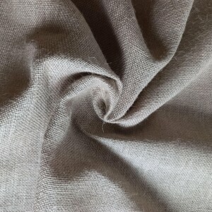 Puede incluir: Primer plano de una tela de yute beige con una textura gruesa y tejida. La tela está doblada y drapeada, creando sombras y reflejos. Las fibras naturales tienen un aspecto ligeramente áspero.