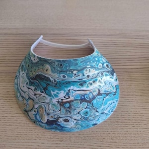 May include: A blue and white sun visor with a swirling abstract pattern. The visor has a white elastic band.