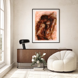 May include: Abstract art print in a black frame. The artwork features a blend of brown and reddish-pink hues, creating a textured, expressive composition. The print is displayed above a wooden cabinet, with a black lamp and a white chair.
