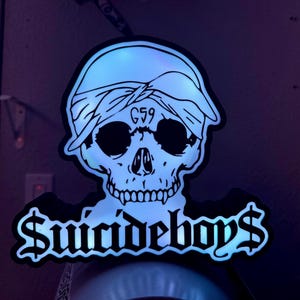 May include: A black and white skull sticker with a bandana and the text "G59" above the eyes. The words "Suicideboys$" are written in a stylized font below the skull.