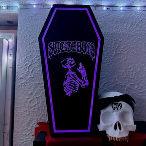 May include: Black coffin-shaped LED light with the text "SUICIDEBOYS" and a purple skeleton praying. A white skull with a black bandana and the text "G59" is next to the coffin.