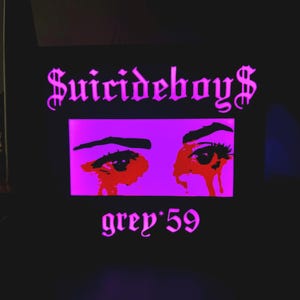 May include: Black graphic featuring the text "Suicideboys" in a gothic font above a purple rectangle with stylized eyes and red tears. Below, the text "grey*59" is also in a gothic font.