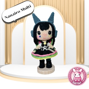 May include: A handmade crochet doll with black hair, blue accents, and a colorful dress. The doll has a round face with large eyes and is standing on a wooden base. The text "Nanairo Multi" is in a speech bubble above the doll.