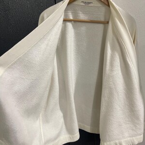 Pu&ograve; includere: Una tazza di ceramica bianca con manico nero e la scritta "But First, Coffee" in nero, in grassetto. La tazza &egrave; appoggiata su una superficie bianca.