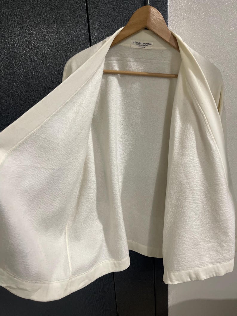 Pu&ograve; includere: Una tazza di ceramica bianca con manico nero e la scritta "But First, Coffee" in nero, in grassetto. La tazza &egrave; appoggiata su una superficie bianca.