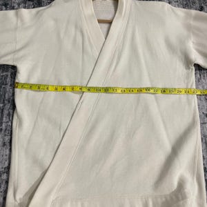 Pu&ograve; includere: Felpa color crema stile avvolgente con scollo a V e maniche corte. Il capo &egrave; misurato con un metro a nastro giallo, che mostra una lunghezza di circa 56 cm.