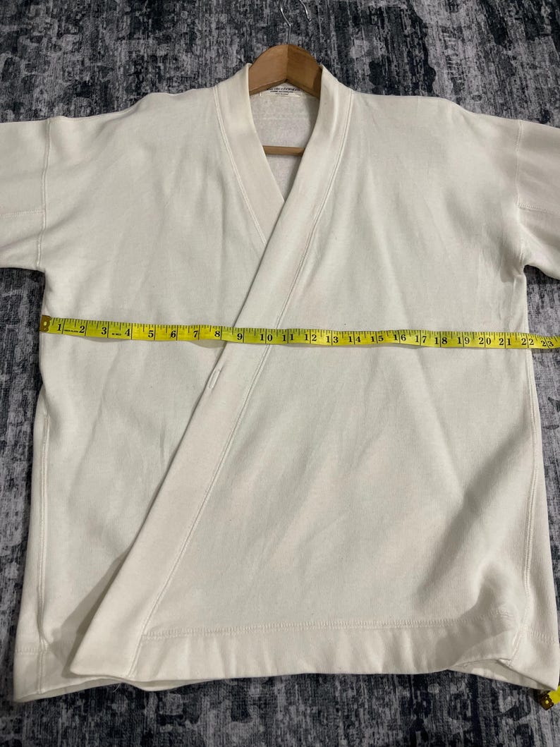 Pu&ograve; includere: Felpa color crema stile avvolgente con scollo a V e maniche corte. Il capo &egrave; misurato con un metro a nastro giallo, che mostra una lunghezza di circa 56 cm.