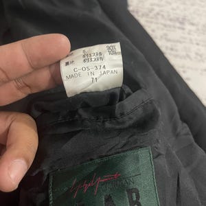 Może przedstawiać: Zbliżenie na wnętrze czarnego ubrania, ukazujące metkę z japońskim tekstem i napisem "MADE IN JAPAN". Na metce widnieją r&oacute;wnież procenty składu tkaniny oraz marka "A.A.R".