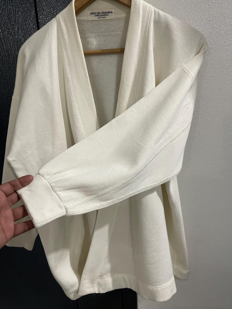 Pu&ograve; includere: Felpa robe de chambre color crema con collo a scialle e maniche lunghe. L'indumento &egrave; realizzato in un materiale morbido e spesso e presenta una vestibilit&agrave; ampia. Il testo "robe de chambre" &egrave; visibile sull'etichetta.