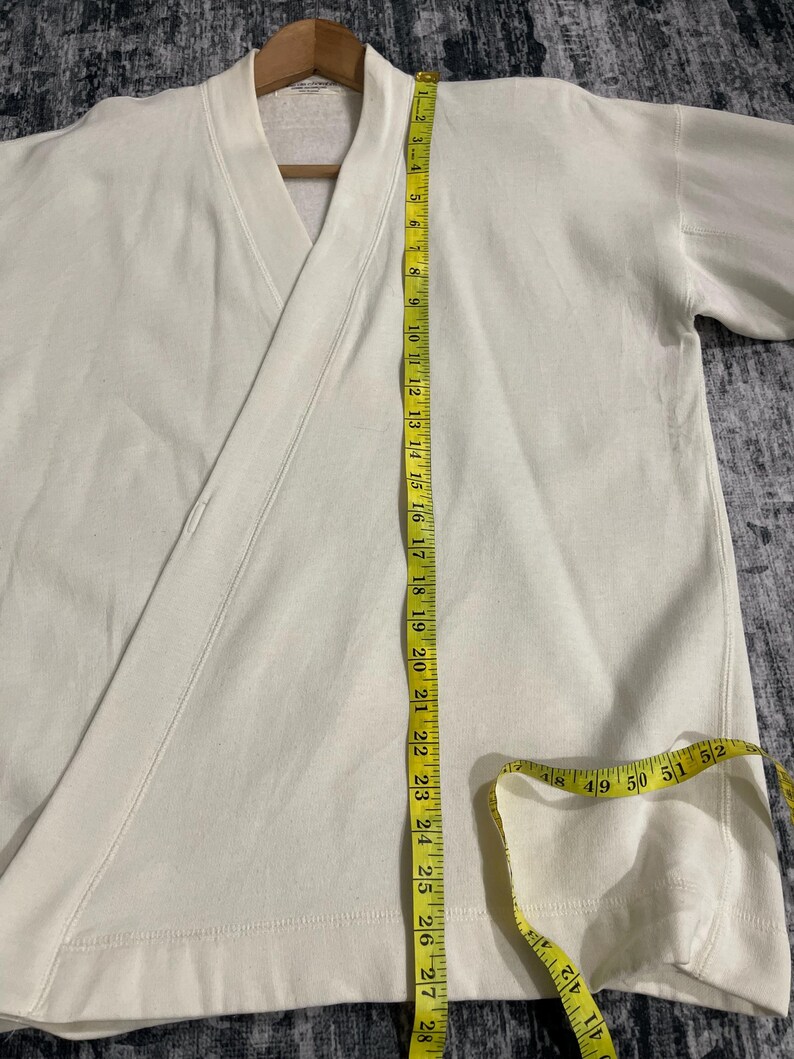 Pu&ograve; includere: Top avvolgente color crema con scollo a V e maniche lunghe. Un metro a nastro giallo &egrave; appoggiato sul capo, mostrando le misure in centimetri. Il top &egrave; realizzato in un materiale morbido, probabilmente cotone.