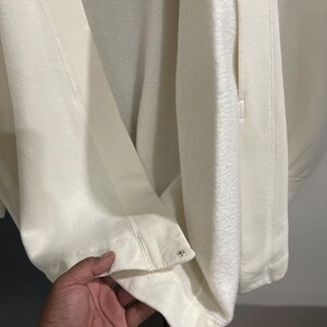 Pu&ograve; includere: Giacca in pile color crema dall'aspetto morbido e strutturato. La giacca presenta una cerniera e borchie decorative in metallo sull'orlo. Il tessuto appare spesso e caldo, adatto alle temperature pi&ugrave; fresche.