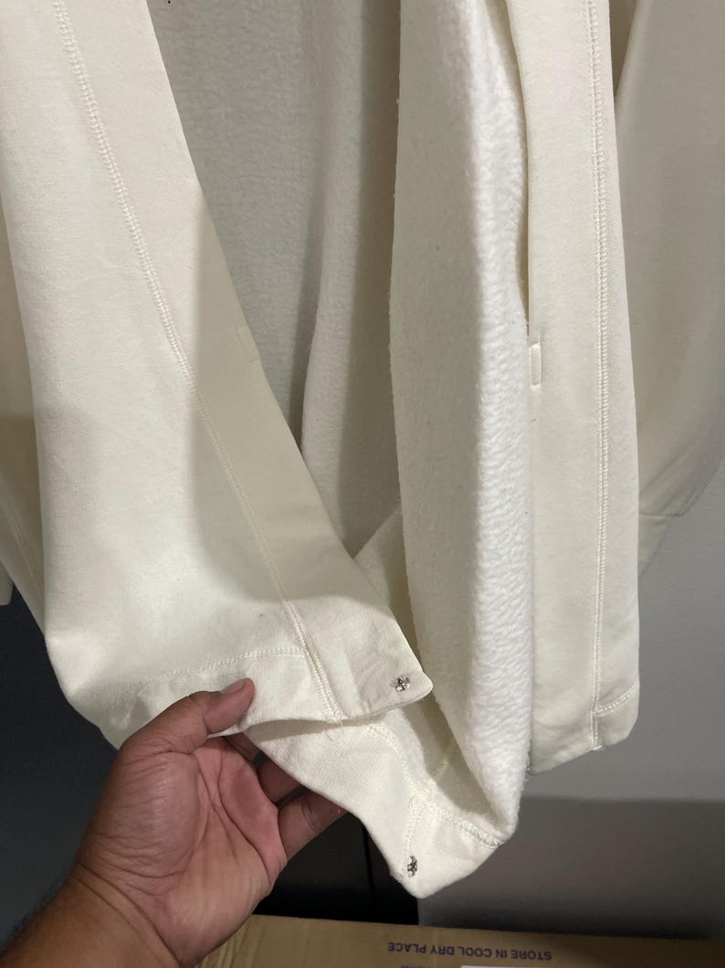 Pu&ograve; includere: Giacca in pile color crema dall'aspetto morbido e strutturato. La giacca presenta una cerniera e borchie decorative in metallo sull'orlo. Il tessuto appare spesso e caldo, adatto alle temperature pi&ugrave; fresche.