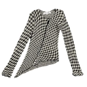 May include: A black and white gingham cardigan with long sleeves. The top features a button-up front and an unusual asymmetrical hem. The label "COMME des GARÇONS" is visible at the neckline. The sleeves have a ruffled cuff.