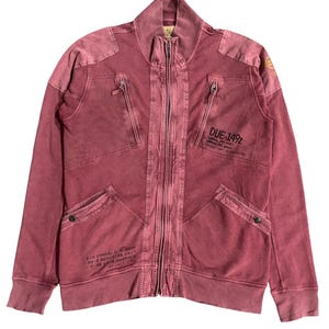 Peut inclure: Veste zipp&eacute;e bordeaux avec un col montant et plusieurs poches. La veste pr&eacute;sente du texte sur le devant et les manches, dont "DUE-149Z" et "AIR FORCE, U.S. ARMY". La veste a un aspect vintage et us&eacute;.