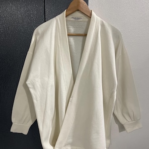 Pu&ograve; includere: Cardigan color crema con apertura frontale e maniche a tre quarti. Il cardigan &egrave; appeso a una gruccia di legno. L'indumento ha una vestibilit&agrave; morbida e un design minimalista, con dettagli di cucitura visibili.