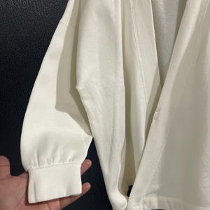Pu&ograve; includere: Cardigan color crema con maniche lunghe e vestibilit&agrave; morbida. Il cardigan presenta uno scollo a V e una chiusura con bottoni. Le maniche hanno polsini a coste. Il tessuto sembra essere un materiale morbido e confortevole.
