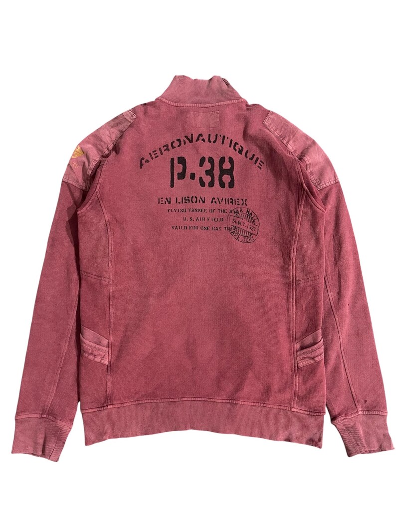 Peut inclure: Sweat-shirt zipp&eacute; rouge vieilli avec le texte "Aeronautique P.38" imprim&eacute; au dos. Le sweat-shirt pr&eacute;sente un col montant, des &eacute;cussons d'&eacute;paule et deux poches avant. Le design de style vintage comprend des d&eacute;tails d&eacute;lav&eacute;s et un aspect vieilli.