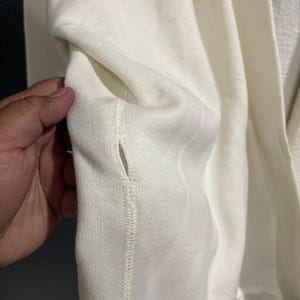 Pu&ograve; includere: Primo piano di una tasca di felpa color crema. La tasca &egrave; cucita nel capo con cuciture visibili. Il tessuto sembra essere un materiale morbido e strutturato. L'immagine mostra l'interno della tasca.