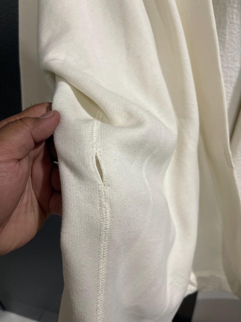 Pu&ograve; includere: Primo piano di una tasca di felpa color crema. La tasca &egrave; cucita nel capo con cuciture visibili. Il tessuto sembra essere un materiale morbido e strutturato. L'immagine mostra l'interno della tasca.