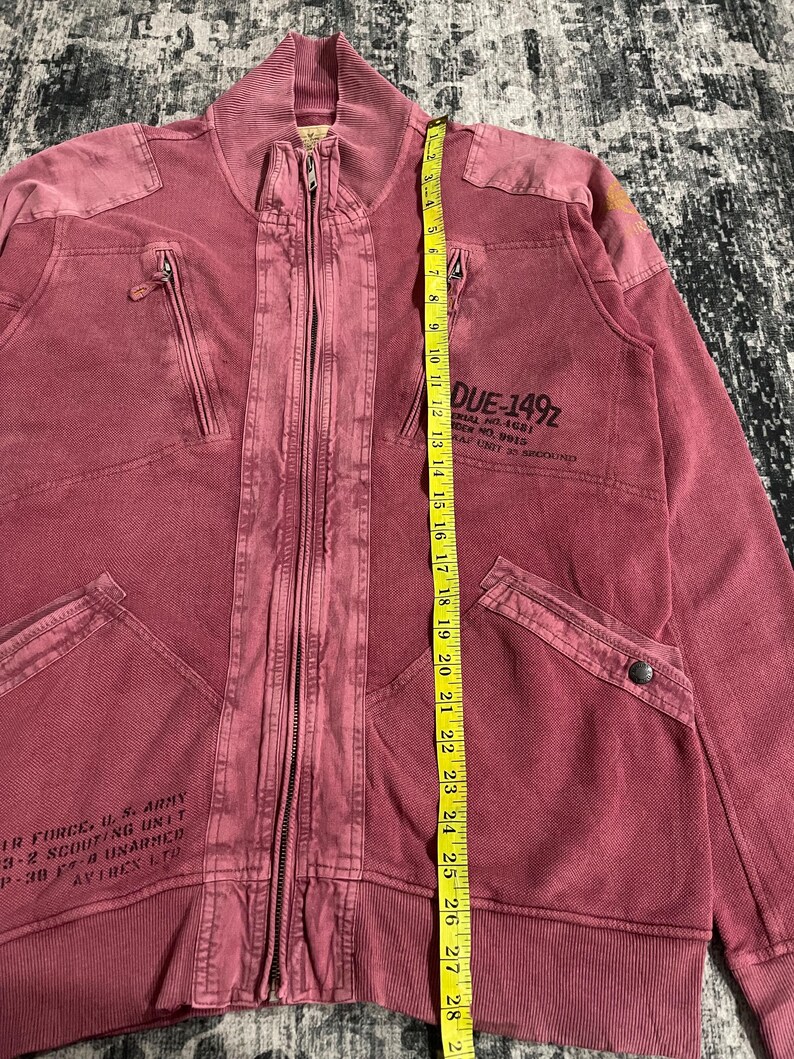 Peut inclure: Veste zipp&eacute;e bordeaux avec plusieurs poches et un col c&ocirc;tel&eacute;. La veste comporte du texte &agrave; l'avant et un m&egrave;tre ruban jaune. La veste mesure environ 74 cm de long.