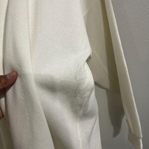 Pu&ograve; includere: Felpa color crema con tasca e maniche lunghe. Il tessuto sembra essere un materiale morbido e di peso medio. Il capo &egrave; presentato su uno sfondo neutro.