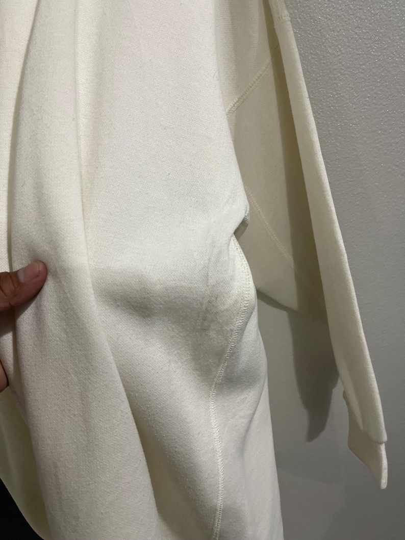 Pu&ograve; includere: Felpa color crema con tasca e maniche lunghe. Il tessuto sembra essere un materiale morbido e di peso medio. Il capo &egrave; presentato su uno sfondo neutro.