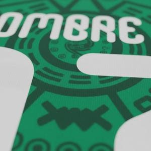 May include: Close-up of a green fabric with white text that reads "OMBRE". The fabric has a detailed pattern in a darker shade of green, featuring geometric and circular designs. The overall aesthetic is bold and graphic.