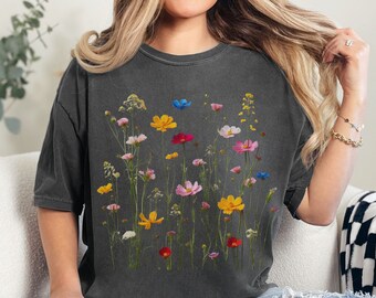 May include: Dark gray t-shirt featuring a colorful floral design. The graphic includes various wildflowers in shades of yellow, pink, red, blue, and white. The shirt has a relaxed fit and short sleeves, perfect for casual wear.