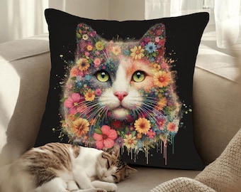 以下が含まれることがあります： カラフルな猫のイラストが描かれた黒いクッション。猫の毛皮は花でできており、背景は黒い塗料の飛沫がかかっています。猫がクッションの前でソファで寝ています。