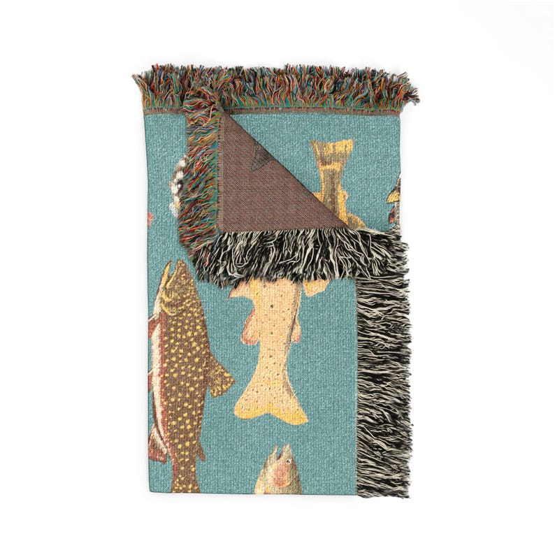 May include: A folded turquoise throw blanket featuring a repeating pattern of various fish illustrations in shades of brown, yellow, and red. The blanket has a fringed edge with a mix of colors. The underside of the blanket is brown.