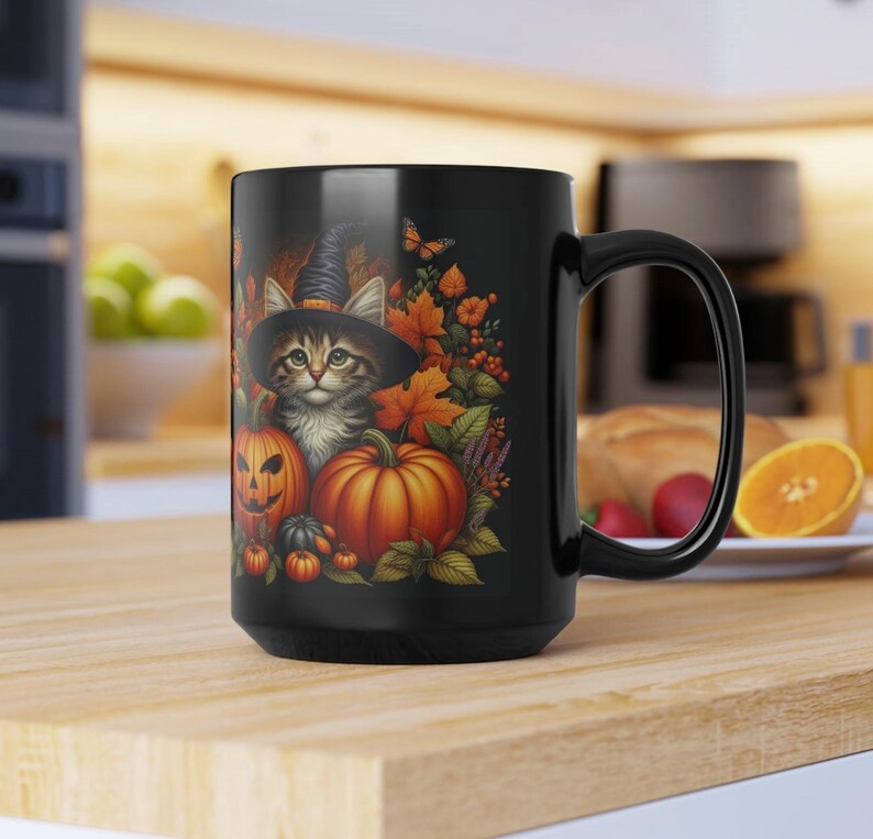 May include: Black ceramic mug featuring a Halloween-themed design. The design includes a kitten wearing a witch hat, pumpkins, and autumn leaves. The mug has a large handle and is sitting on a wooden surface.